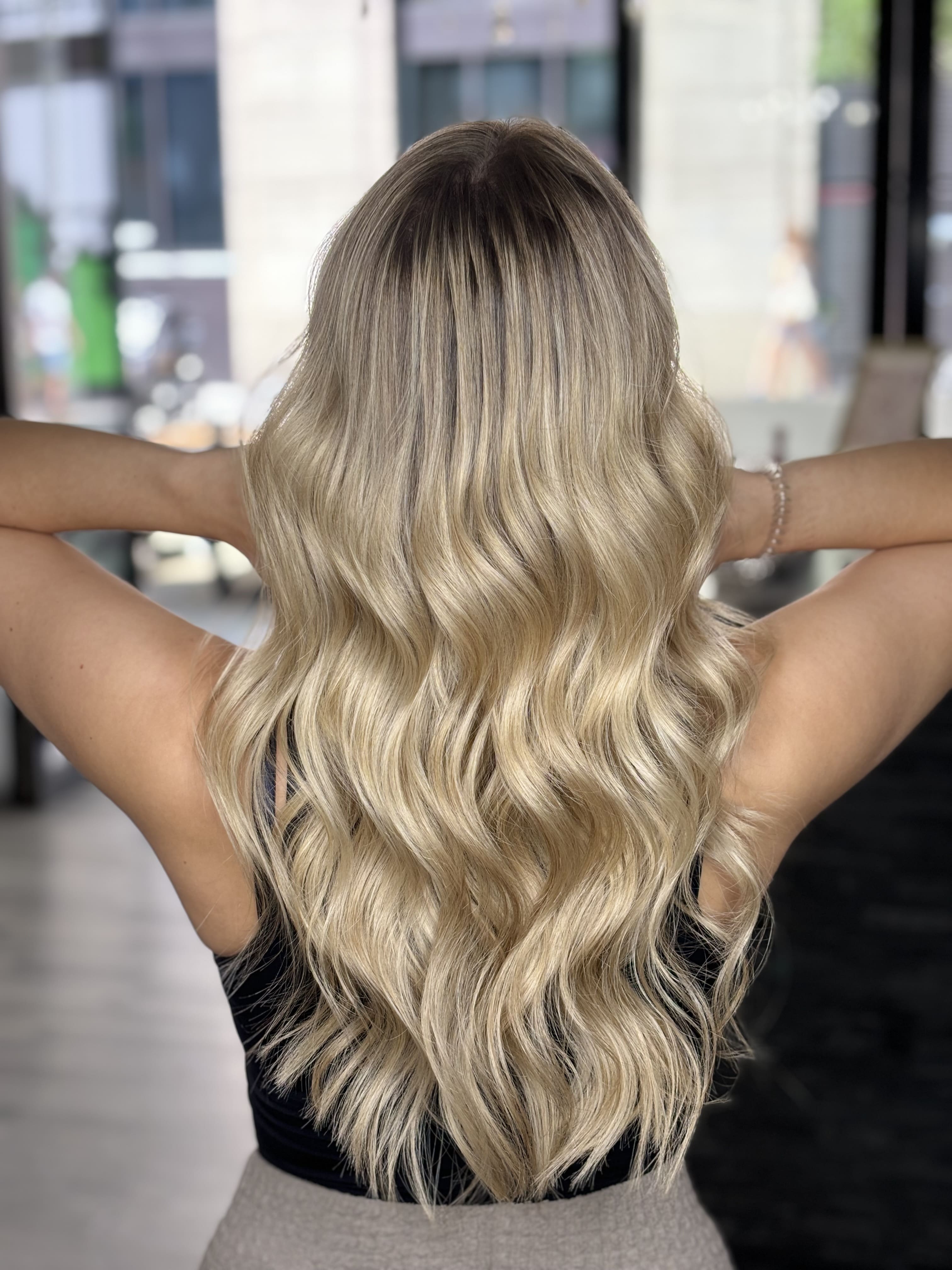 Eine Frau mit langen, gewellten blondierten Haaren steht mit dem Rücken zur Kamera