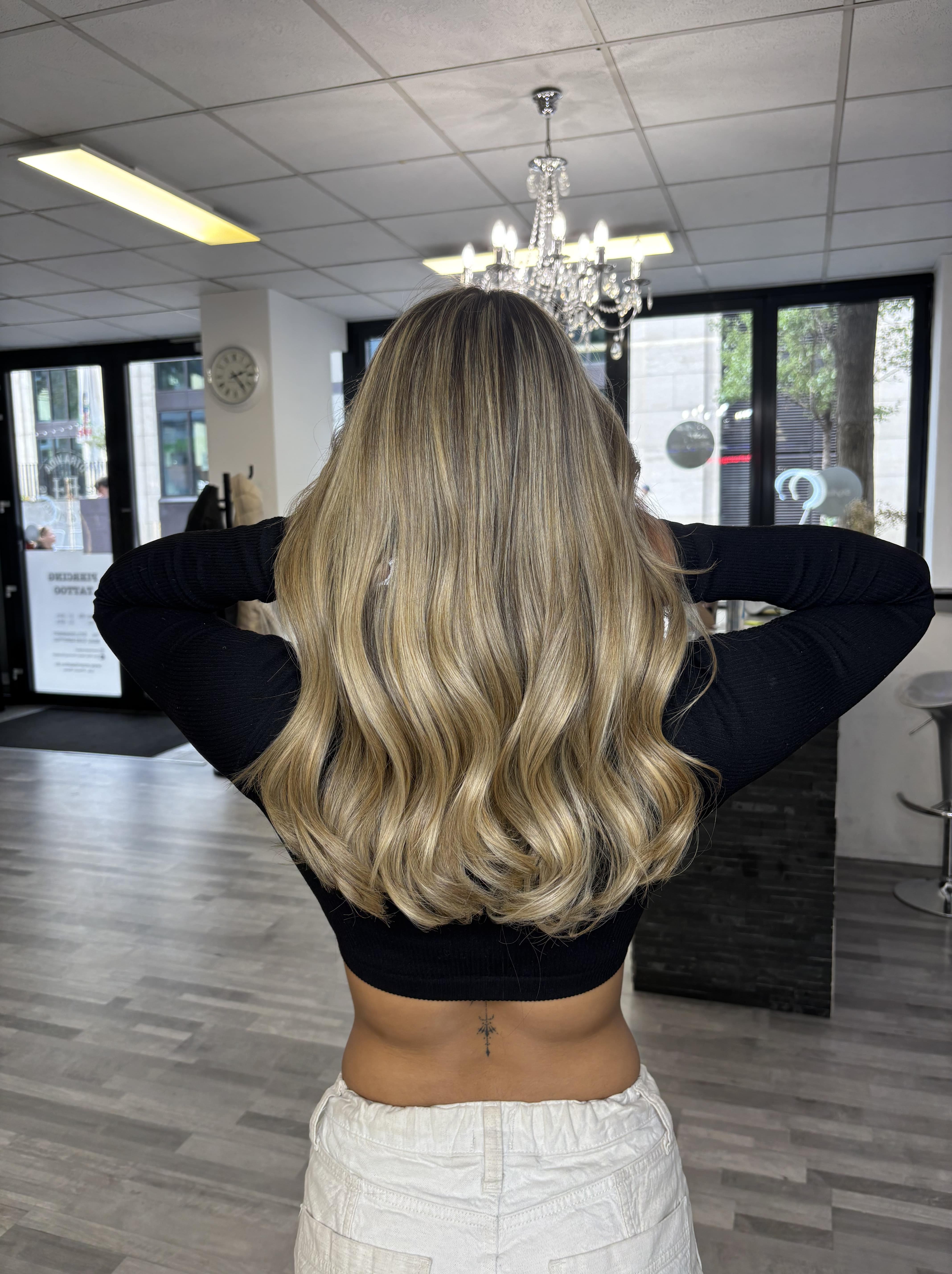 Eine Frau mit langen, gewellten blonden Haaren zeigt stolz ihre frische Frisur