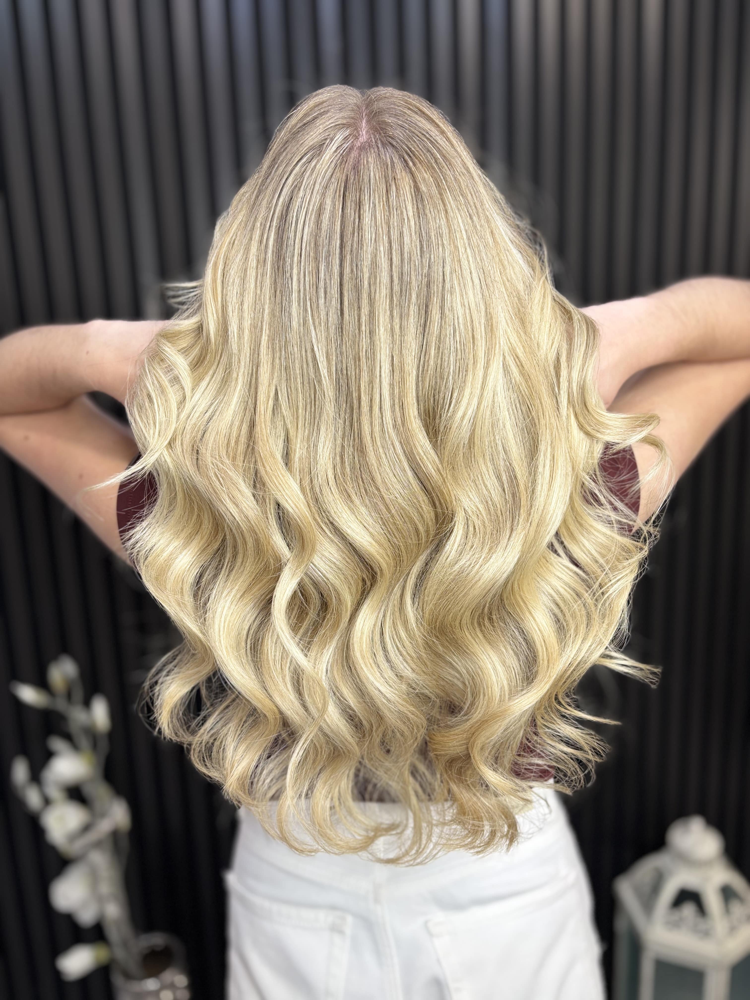 Eine Person mit langen welligen blonden Haaren steht vor einer dunklen Wand